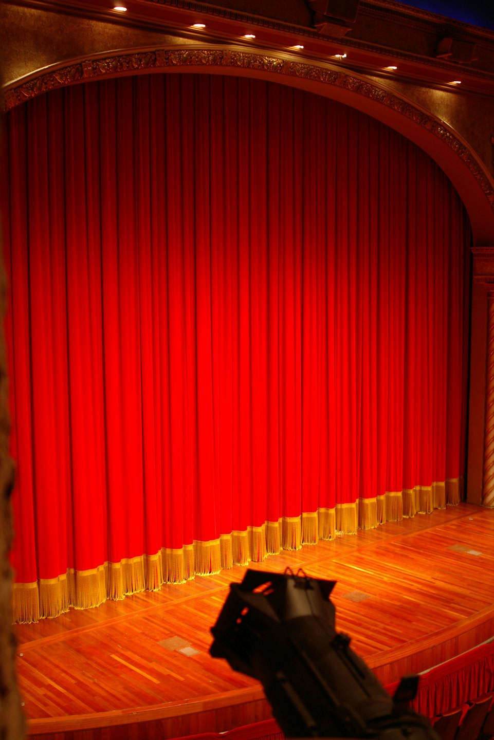 Empty theater stage with red curtains and gold trim.